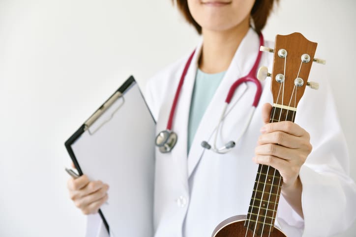 médecin femme avec un stéthoscope autour du cou elle teint dans un main un porte-blocs rigide avec des feuilles blanches et un stylo et dans l'autre main une guitare